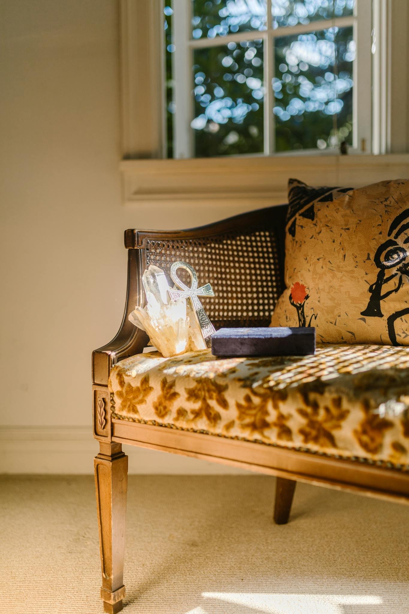A vintage decorative couch next to a window, bathed in warm sunlight, creating a cozy indoor setting.