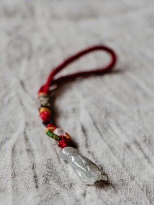 Close-up of an elegant gemstone amulet with a red lucky knot on textured fabric, exuding charm and artistry.